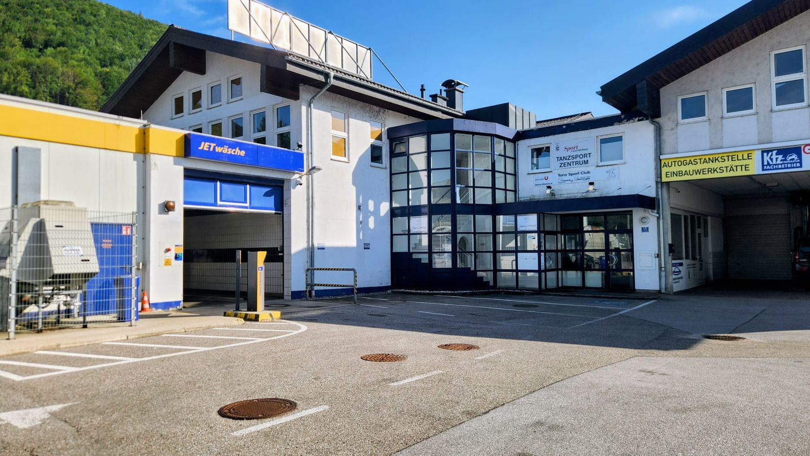 Außenansicht des Gebäudes Wiener Bundesstraße 15: weißes Haus mit verglastem, blau gerahmtem Eingangsbereich und der Aufschrift „Tanzsport Zentrum“, davor ein Parkplatz